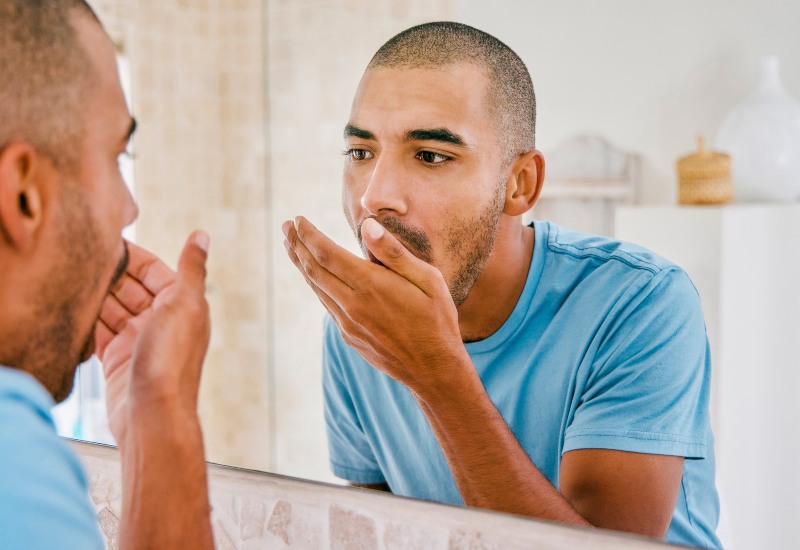A man inspects his breath in the mirror to learn about bad breath causes & prevention in Millersburg