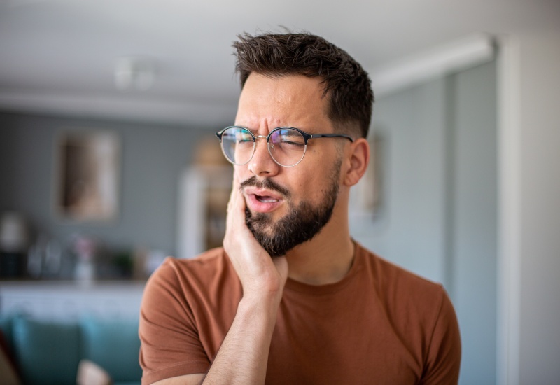 A man holding his cheek in pain, showing discomfort from wisdom teeth removal in Millersburg, OH