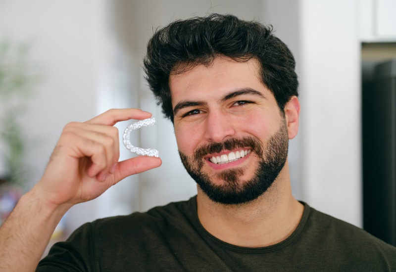 A smiling man holding a clear aligner, promoting Invisalign Clear Aligners in Millersburg, OH