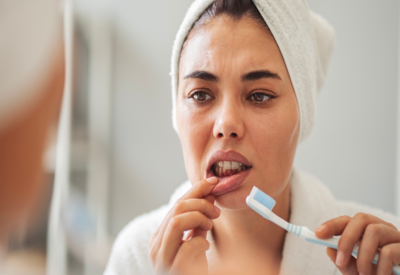 A woman examines her gums in a mirror while brushing, addressing bleeding gums in Millersburg, OH